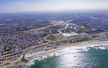 Aerial view of San Dieguito Lagoon, with a large patch of green salt marsh between dense city and the Pacific Ocean. 