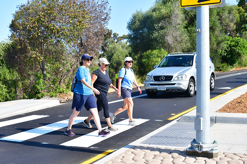 Three women cross Redwood Street in San Diego using the new crosswalk while a gray car waits for them to cross.