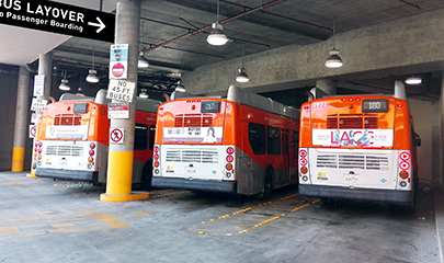 Three red buses diagonally parked next to each other in marked spaces of a cement parking garage.